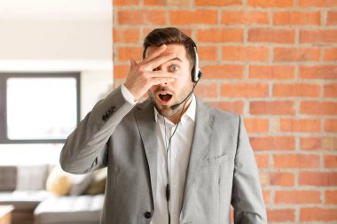 Yakışıklı pazarlamacı şok olmuş, korkmuş ya da korkmuş görünüyor. Yüzü elle kaplanmış ve parmaklarının arasından gizlice bakıyor.