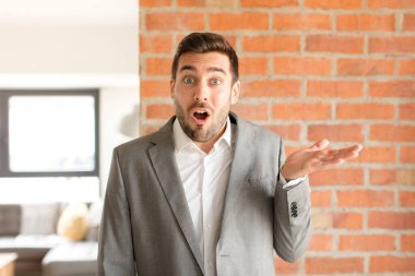 Yakışıklı işadamı şaşırmış ve şok olmuş görünüyor, çenesi düşmüş ve eli açık bir nesneyi tutuyor.