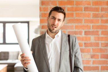 handsome architect feeling puzzled and confused, with a dumb, stunned expression looking at something unexpected
