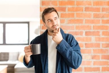 Yakışıklı bir adam mutlu, kendinden emin bir ifadeyle gülümsüyor. Elleri çenesinde, merak ediyor ve yan tarafa bakıyor.