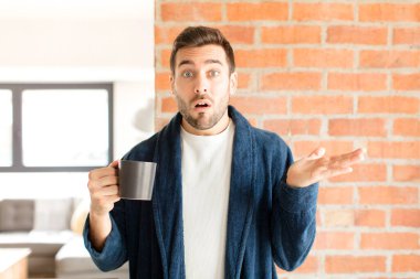 Yakışıklı adam şaşırmış ve şoka uğramış görünüyor, çenesi düşmüş, bir objeyi elinde açık bir elle tutuyor.