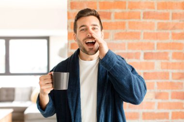 Yakışıklı adam mutlu, heyecanlı ve pozitif hissediyor. Elleri ağızda, bağırarak bağırıyor.