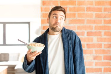 Yakışıklı adam omuz silkiyor, şaşkın ve kararsız hissediyor, kolları bağlı ve şaşkın bir şekilde şüpheye düşüyor.