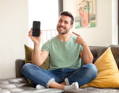 Yakışıklı adam kendinden emin bir şekilde gülümsüyor. Geniş bir gülümseme, pozitif, rahat, tatmin olmuş bir tavır sergiliyor.