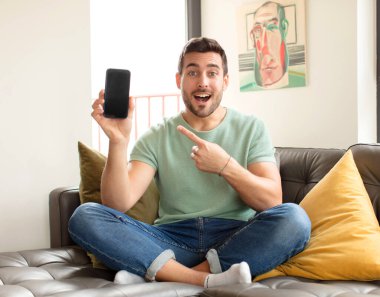 Yakışıklı adam neşeyle gülümsüyor, mutlu hissediyor ve yan ve yukarı doğru işaret ediyor, fotokopi uzayındaki nesneleri gösteriyor.