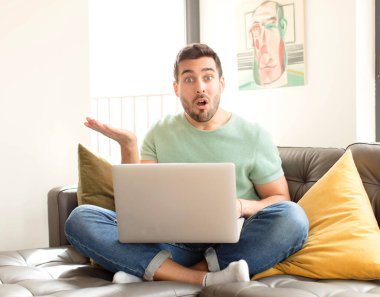 Yakışıklı adam şaşırmış ve şoka uğramış görünüyor, çenesi düşmüş, bir objeyi elinde açık bir elle tutuyor.