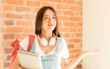 Neşeli bir şekilde gülümsüyor, mutlu hissediyor ve bir konsepti fotokopi uzayında avuç içiyle gösteriyor.