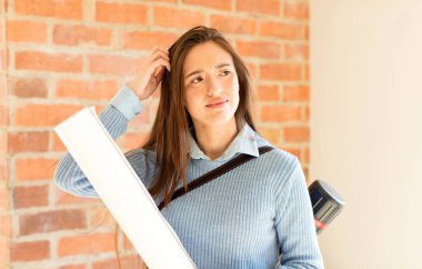 Güzel mimar şaşkın ve kafası karışmış hissediyor, başını kaşıyor ve yan tarafa bakıyor.