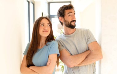 Genç çift omuz silkiyor, şaşkın ve kararsız hissediyor, kolları bağlı ve şaşkın bir şekilde şüpheye düşüyor.