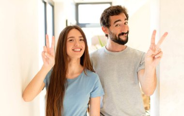 Genç çift gülümsüyor ve arkadaş canlısı görünüyor. İki ya da iki numarayı gösteriyor. Elleri önde, geri sayıyor.