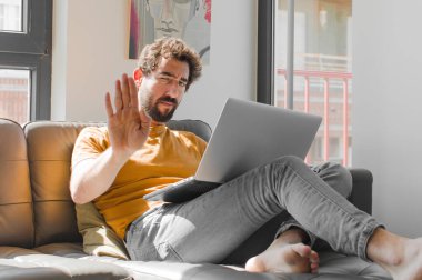 Genç sakallı adam ciddi, sert, hoşnutsuz ve kızgın görünüyor. Avuç içini açıp dizüstü bilgisayarda dizüstü bilgisayarla hareket etmeyi kesiyor.