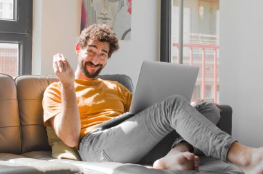 Genç sakallı adam sana borcunu ödemeni söyleyerek kapiş ya da para hareketi yapıyor! Dizüstü bilgisayarlı kanepe konsepti.