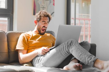 Genç sakallı adam agresif bir şekilde bağırıyor, sinirli, sinirli, öfkeli ya da sinirli görünüyor, dizüstü bilgisayarla hayır diye bağırıyor.