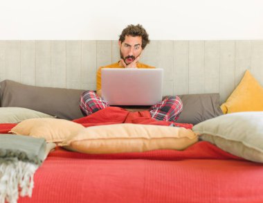 Ağzı ve gözleri açık, eli çenesinde genç sakallı bir adam. Hoş olmayan bir şok geçiriyor.