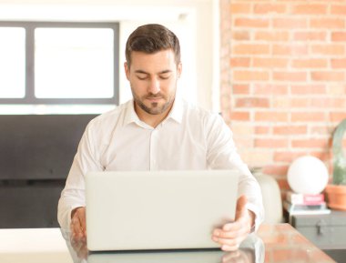 Evde dizüstü bilgisayar kullanan genç ve yakışıklı bir adam.