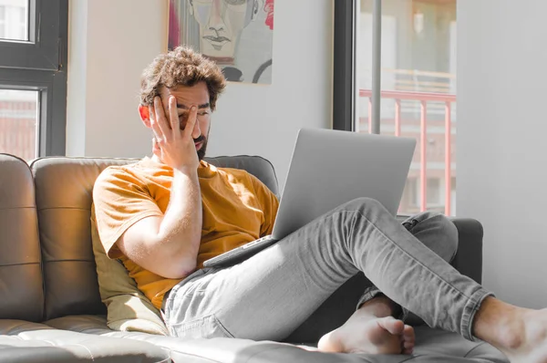 Genç sakallı bir adam sıkıcı, sıkıcı ve sıkıcı bir işin ardından sıkılmış, hayal kırıklığına uğramış ve uykulu hissediyor. Dizüstü bilgisayar konseptinde dizüstü bilgisayarla el ele tutuşuyor.