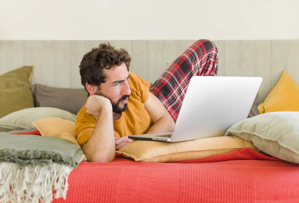 young bearded man on a bed with a laptop