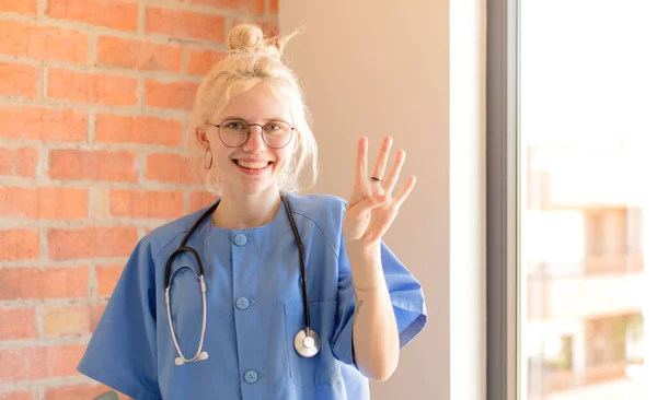 Ładna Pielęgniarka Uśmiecha Się Wygląda Przyjaźnie Pokazuje Numer Cztery Lub — Zdjęcie stockowe