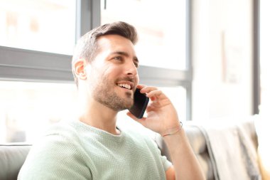 Genç yakışıklı adam akıllı telefonunu evde kullanıyor.