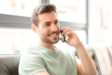 Genç yakışıklı adam akıllı telefonunu evde kullanıyor.