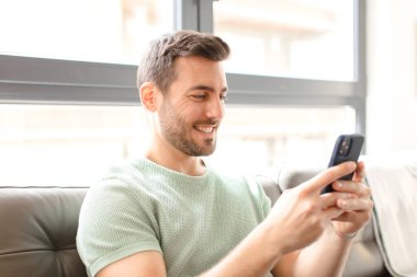 Genç yakışıklı adam akıllı telefonunu evde kullanıyor.