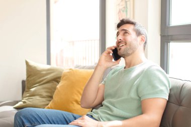 Genç yakışıklı adam akıllı telefonunu evde kullanıyor.