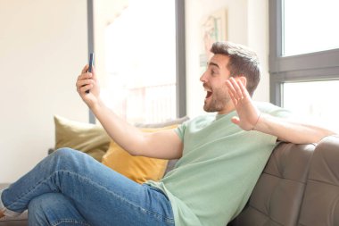 Genç yakışıklı adam akıllı telefonunu evde kullanıyor.