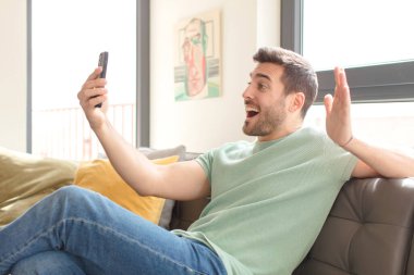 Genç yakışıklı adam akıllı telefonunu evde kullanıyor.