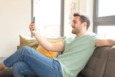 Genç yakışıklı adam akıllı telefonunu evde kullanıyor.