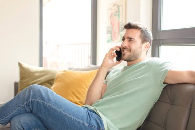 Genç yakışıklı adam akıllı telefonunu evde kullanıyor.