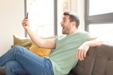 Genç yakışıklı adam akıllı telefonunu evde kullanıyor.