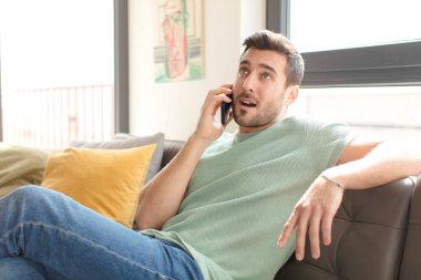 Genç yakışıklı adam akıllı telefonunu evde kullanıyor.