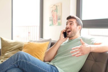 Genç yakışıklı adam akıllı telefonunu evde kullanıyor.