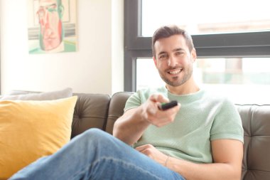 Genç yakışıklı bir adam televizyon kanalını seçiyor.