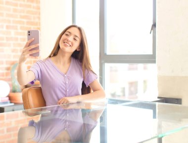 Genç ve güzel bir kız cep telefonuyla masada oturuyor.