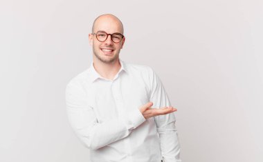 Kel adam mutlu bir şekilde gülümsüyor, mutlu hissediyor ve fotokopi alanında avucuyla bir konsept gösteriyor.