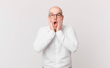 Kel adam şok olmuş ve korkmuş hissediyor, ağzı açık ve elleri yanaklarında korkmuş görünüyor.