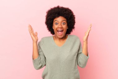 Afro siyah kadın mutlu, heyecanlı, şaşırmış ya da şok olmuş hissediyor, gülümsüyor ve hayrete düşüyor.