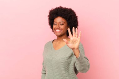 Afro siyah kadın gülümsüyor ve arkadaş canlısı görünüyor, 5 ya da 5 numarayı gösteriyor, eli önde, geriye doğru sayıyor