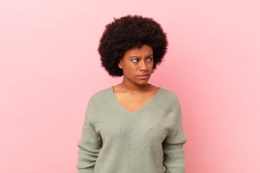 Afro siyahi kadın üzgün, üzgün ya da kızgın hissediyor ve olumsuz bir tavırla yan yana bakıyor, anlaşmazlık içinde kaşlarını çatıyor.