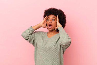 Afro siyahi kadın mutlu, heyecanlı ve şaşırmış hissediyor, iki eli yüzü yana bakıyor.