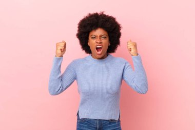 Afro siyah kadın öfkeli bir ifadeyle ya da yumruklarıyla başarıyı kutlarken agresif bir şekilde bağırıyor.