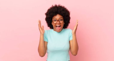 Afro siyah kadın mutlu, heyecanlı, şaşırmış ya da şok olmuş hissediyor, gülümsüyor ve hayrete düşüyor.