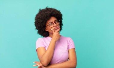 Afro siyah kadın düşünüyor, kuşkulu ve şaşkın hissediyor, farklı seçeneklerle, hangi kararı vereceğini merak ediyor.