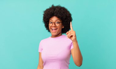 Afro siyah kadın bir fikri fark ettikten sonra mutlu ve heyecanlı bir dahi gibi hissediyor, neşeli bir şekilde parmağını kaldırıyor, eureka!