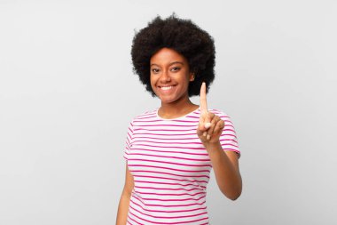 Afro siyah kadın gülümsüyor ve arkadaş canlısı görünüyor, bir numarayı gösteriyor veya ilk eli önde, geriye doğru sayıyor.