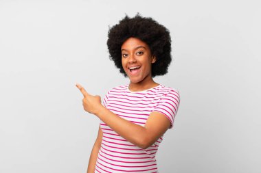 Afro siyah kadın heyecanlı ve şaşırmış görünüyor. Yana ve yukarı doğru uzayı gösteriyor.