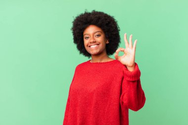 Afro siyah kadın kendini mutlu, rahat ve tatmin olmuş hissediyor. Onayını iyi bir hareketle gösteriyor. Gülümsüyor.