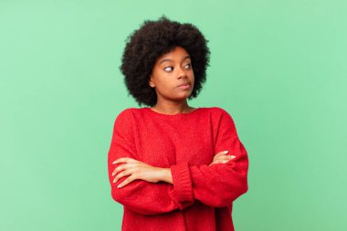 Afro siyah kadın omuz silkiyor, kafası karışık ve kararsız, kolları bağlı ve şaşkın görünüyor.