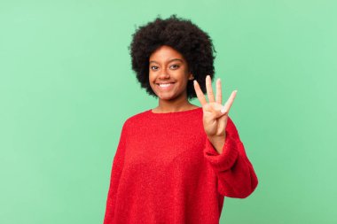 Afro siyah kadın gülümsüyor ve arkadaş canlısı görünüyor, 4 ya da 4 numarayı gösteriyor, eli önde, geriye doğru sayıyor.